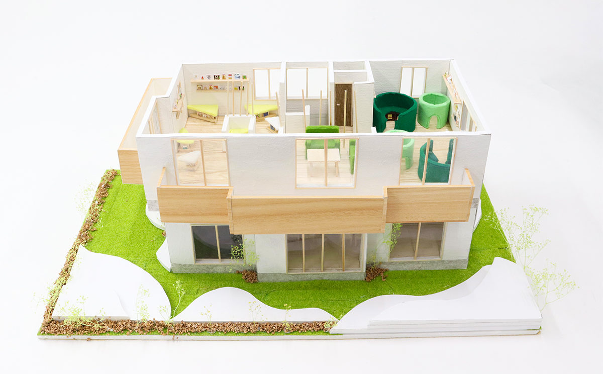 建物全体模型：屋根を取り外しした状態です。芝生の緑色と外壁の白色のコントラストが映え、家具や窓枠が茶色で自然でリラックスできる雰囲気を醸し出しています。